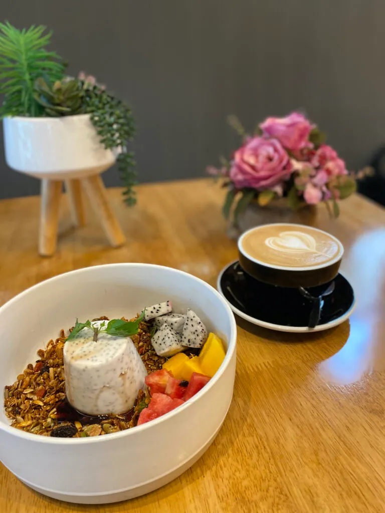 Set chia pudding on a bed of granola and tropical fruit next to a latte with heart shaped latte art at Poached Breakfast Cafe, Chalong, Phuket. The best latte in Phuket.