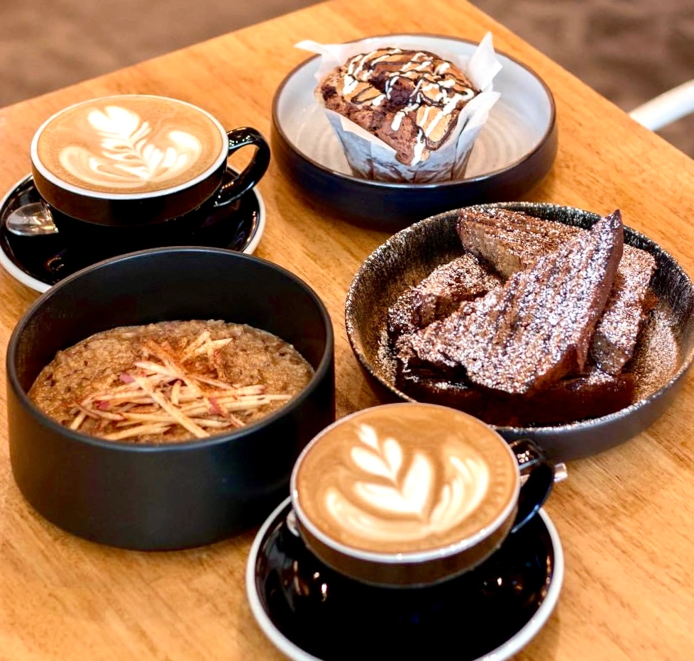 2 Lattes with beautiful latte art, some amazing looking spiced apple porridge, a breakfast muffin and a bowl of amazing banana bread in individual bowls at at Poached Breakfast Cafe, Chalong, Phuket, Thailand. Healthy Breakfast in Chalong and the best fresh food in Chalong.