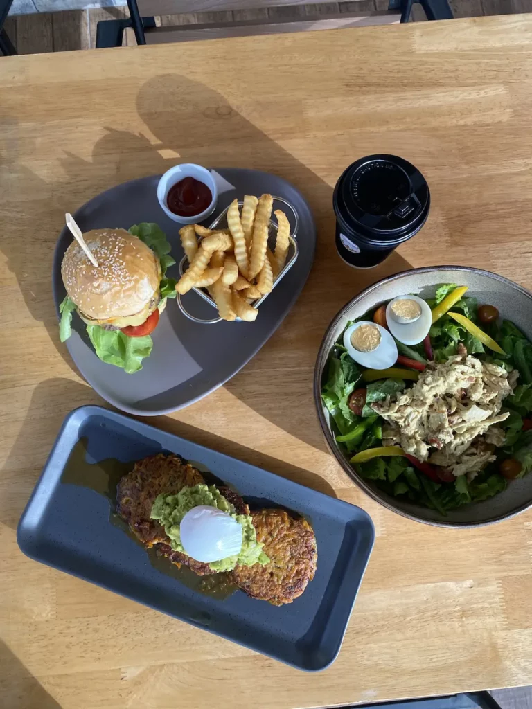 Burger with chips, fritters topped with smashed avocado and a yummy chicken salad on a table at the best place to start sightseeing in Chalong: Poached Breakfast Cafe, Chalong, Phuket, Thailand