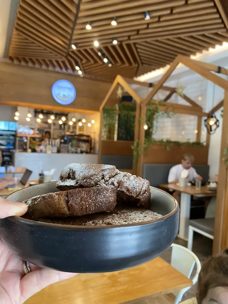 Someone holding a banana bread in front of a sign for Poached breakfast cafe, the number one contender on our ultimate Phuket breakfast guide. At Poached Breakfast Cafe, Chalong, Phuket, Thailand.