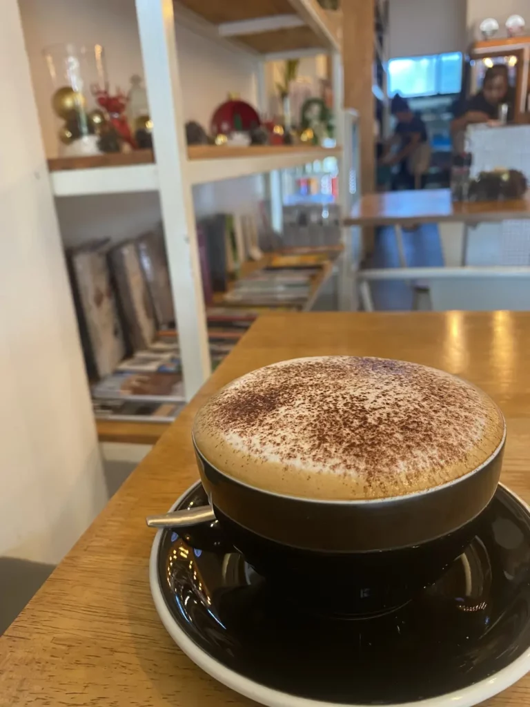 Frothy cappuccino in front of a festive bookshelf at the spot with the best all day breakfast in Phuket: Poached Breakfast Cafe, Chalong, Phuket, Thailand