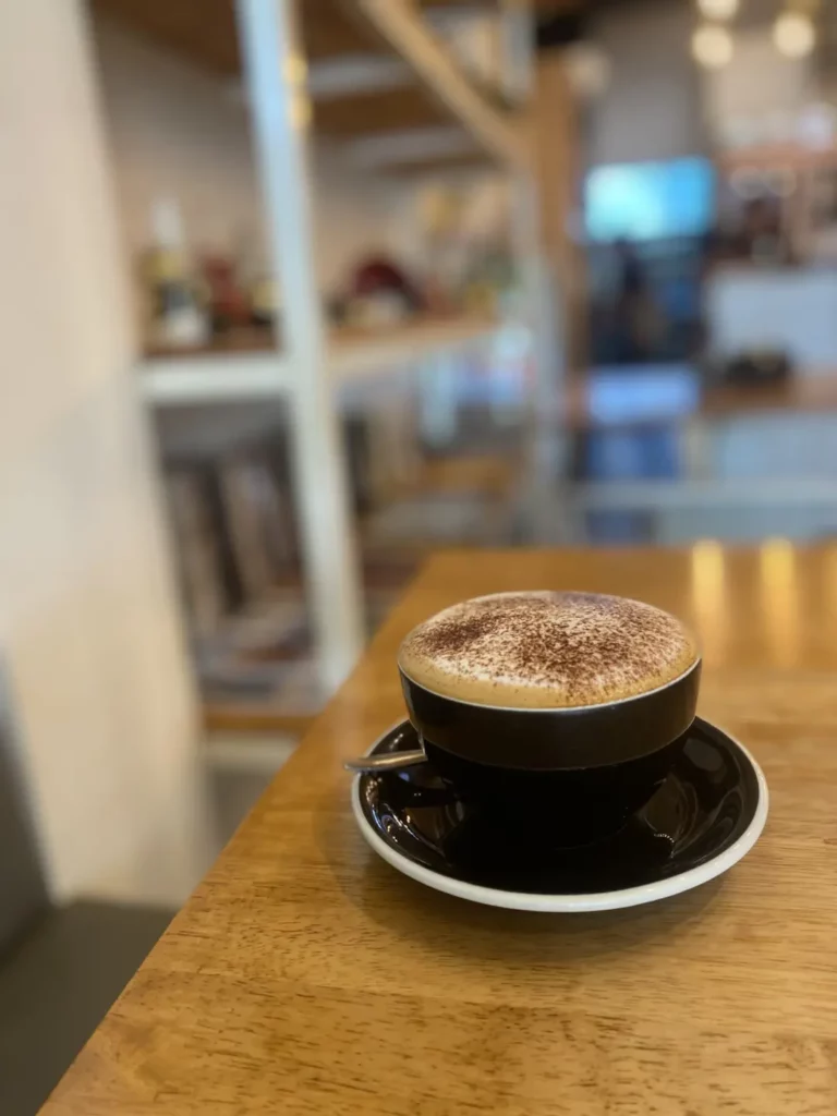 Cappuccino in the foreground with bookshelves in the background at Poached Breakfast Cafe: one of the best holiday experiences in Chalong, Phuket, Thailand