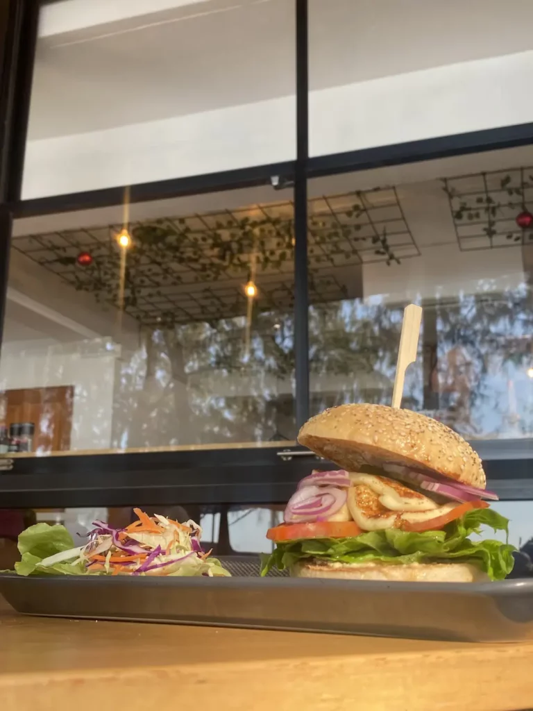 Halloumi bagel on a table with tomatoes, onions, lettuce and a side salad at the number one spot in our backpacker food guide in Chalong - Poached Breakfast Cafe, Chalong, Phuket, Thailand