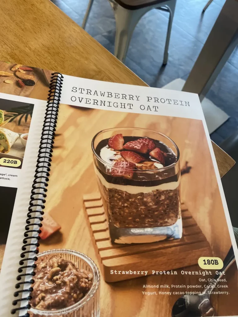 A photo of the menu with overnight oats that are high in protein and topped with strawberries and chocolate at the number one spot in our backpacker food guide in Chalong - Poached Breakfast Cafe, Chalong, Phuket, Thailand