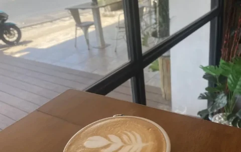 Perfect latte art of a leaf on a latte in a small mug next to a large window at the spot with the best mocha in Chalong: Poached Breakfast Cafe, Chalong, Phuket Thailand