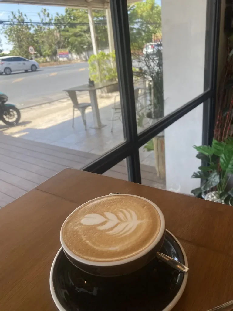 Perfect latte art of a leaf on a latte in a small mug next to a large window at the spot with the best mocha in Chalong: Poached Breakfast Cafe, Chalong, Phuket Thailand