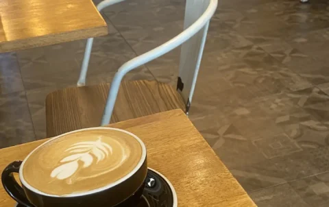 Latte with latte art on a wooden table indoors. The perfect alternative to an iced coffee near Chalong. Only at Poached Breakfast Cafe, Chalong, Phuket, Thailand