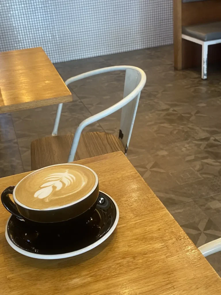 Latte with latte art on a wooden table indoors. The perfect alternative to an iced coffee near Chalong. Only at Poached Breakfast Cafe, Chalong, Phuket, Thailand