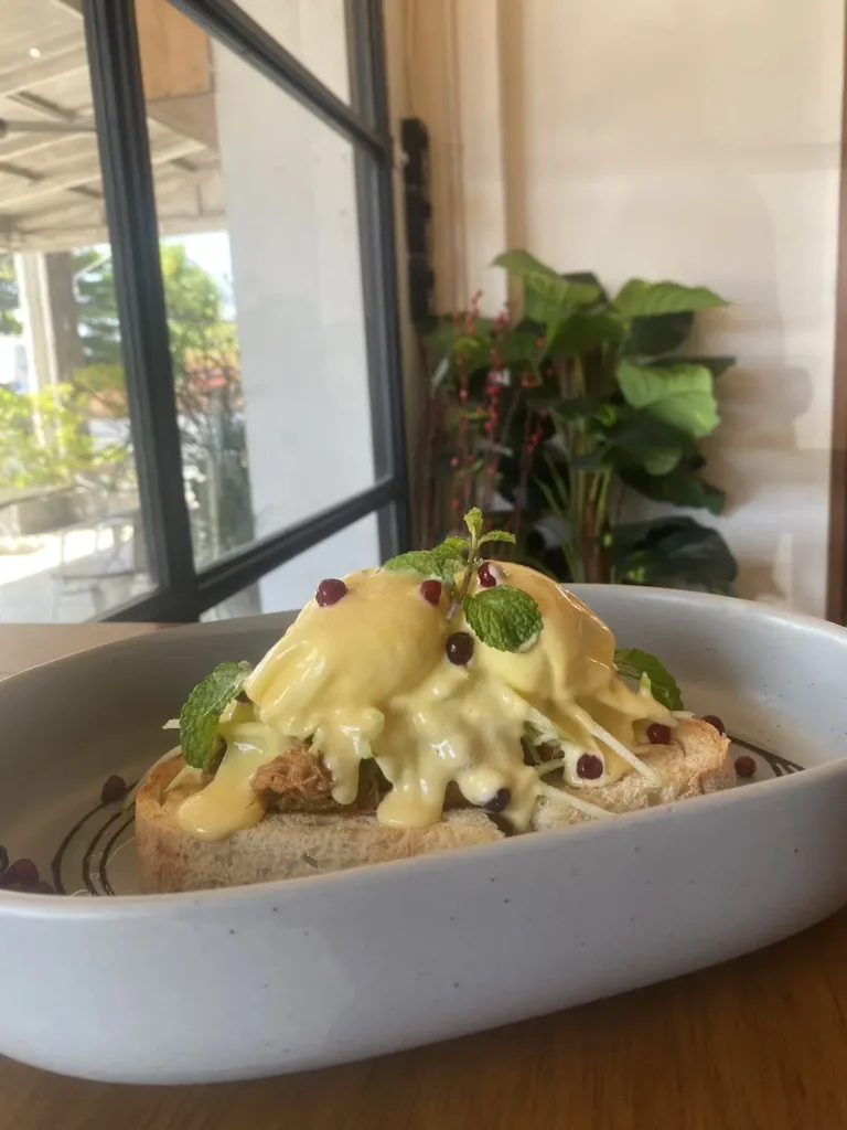 Pulled pork eggs benedict with a hollandaise sauce on top and little pomegranate seeds in front of a window. A delicious alternative to a fresh salad in Chalong that can only be found at Poached Breakfast Cafe, Chalong, Phuket, Thailand