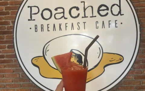 Someone holding a watermelon smoothie in a glass with a straw and slice of watermelon in front of the Poached Breakfast Cafe sign. A delicious companion to a fresh salad in Chalong that can only be found at Poached Breakfast Cafe, Chalong, Phuket, Thailand