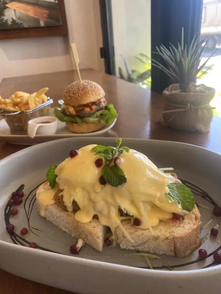 Pulled pork eggs benedict in the foreground and a spicy burger in Chalong in the background at Poached Breakfast Cafe, Chalong, Phuket, Thailand