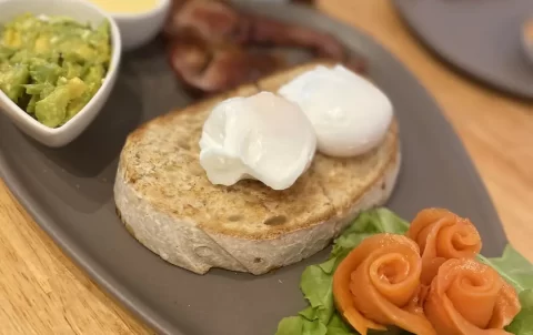 A plate with smoked salmon, sourdough bread, crispy canadian bacon, two poached eggs, smashed avocado and hollandaise sauce. The most delicious bacon in Nai Harn can be found at Poached Breakfast Cafe Rawai, Phuket, Thailand