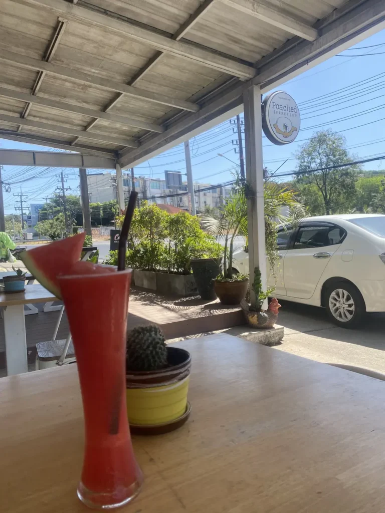 Watermelon smoothie with a slice of watermelon perched on the side of a tall glass. Served on a table outside of our cafe. This is the perfect accompaniment to an avocado breakfast in Chalong. Only at Poached Breakfast Cafe, Chalong, Phuket, Thailand