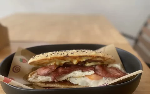 Bacon and egg roll with seeded bun on a table at Poached Breakfast Cafe Rawai, conveniently located near the best resorts near Nai Harn