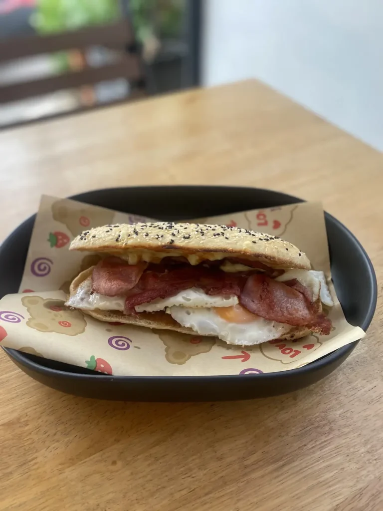 Bacon and egg sandwich on some paper in a shallow bowl at the number one place on the Phuket Travel Guide: Poached Breakfast Cafe, Chalong, Phuket, Thailand