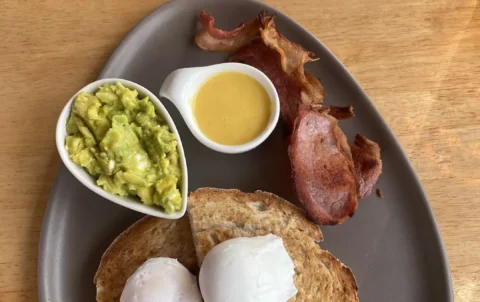 Smashed avo, 2 poached eggs, sourdough bread, bacon and hollandaise sauce on a plate. The best meal to eat before a day of island hopping in Phuket.