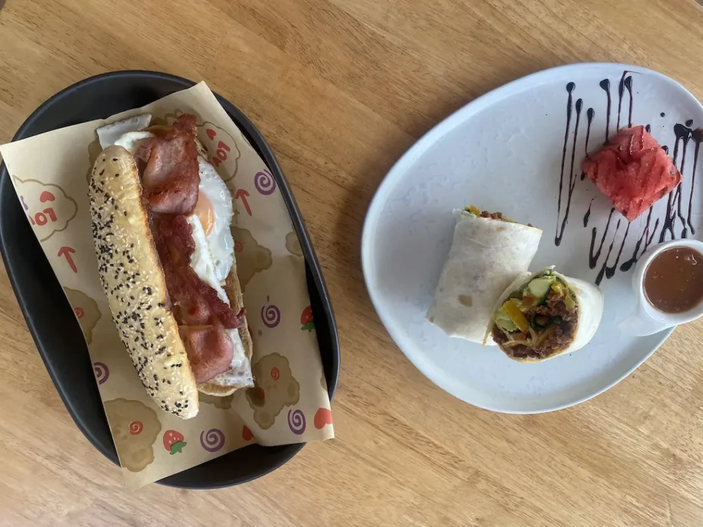 Egg and bacon sandwich with a spicy sausage wrap on a table. Only at the best spot to see before you head to one of the amazing islands to visit near Phuket: Poached Breakfast Cafe, Chalong, Phuket, Thailand