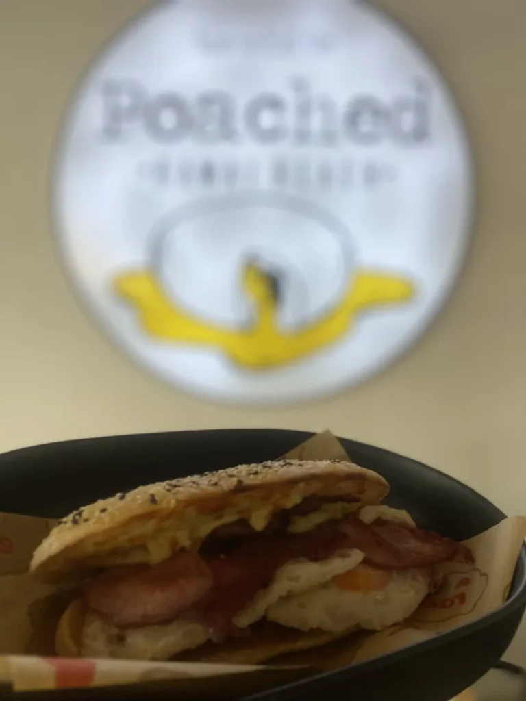 Bacon and egg sandwich in front of a blurry sign at one of the best indoor 
attractions in Phuket: at Poached Breakfast Cafe , Chalong, Phuket, Thailand