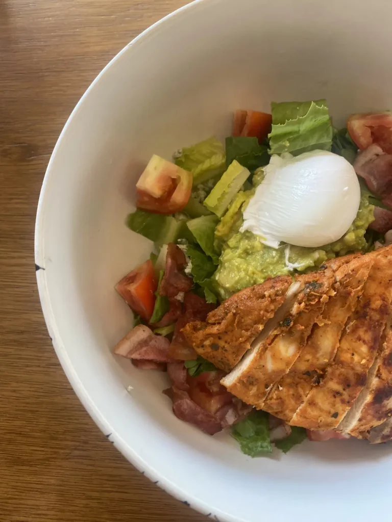 A close up photo of a bowl of chicken cobb salad with bacon, tomato, lettuce, a poached egg, blue cheese and smashed avocado at the best place to fuel up before a day of snorkelling in Phuket - Poached Breakfast Cafe, Chalong, Phuket, Thailand