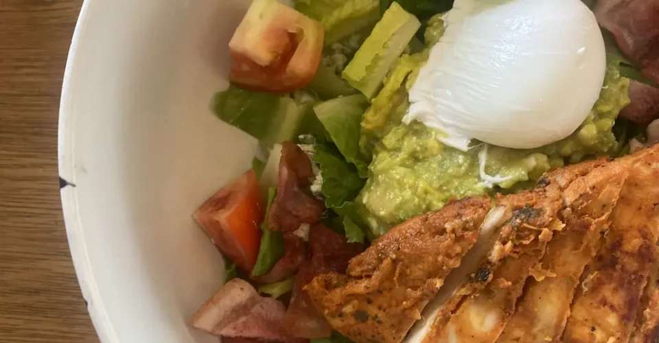 A close up photo of a bowl of chicken cobb salad with bacon, tomato, lettuce, a poached egg, blue cheese and smashed avocado at the best place to fuel up before a day of snorkelling in Phuket - Poached Breakfast Cafe, Chalong, Phuket, Thailand